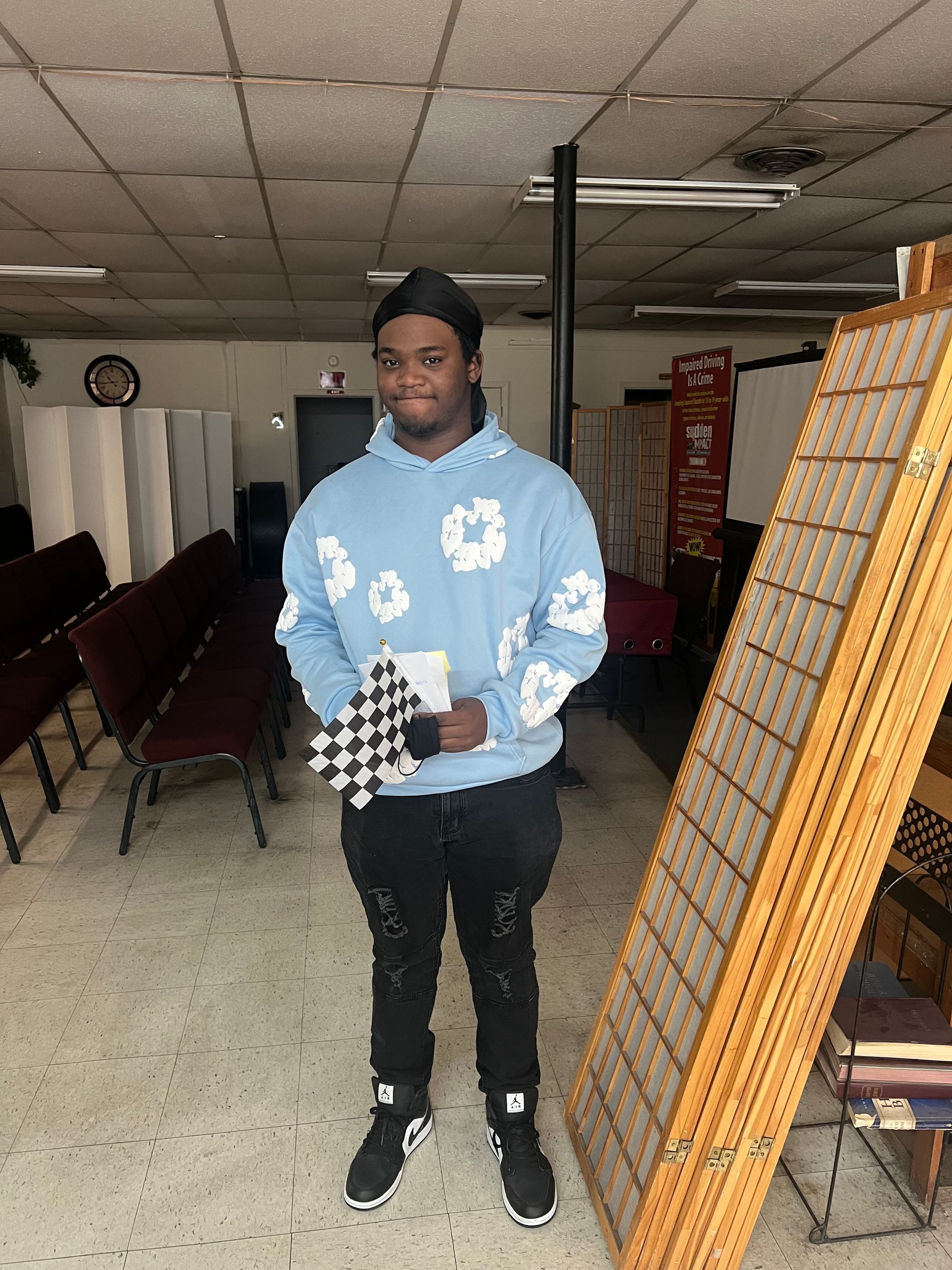A man in a blue hoodie is standing in a room holding a checkered flag.