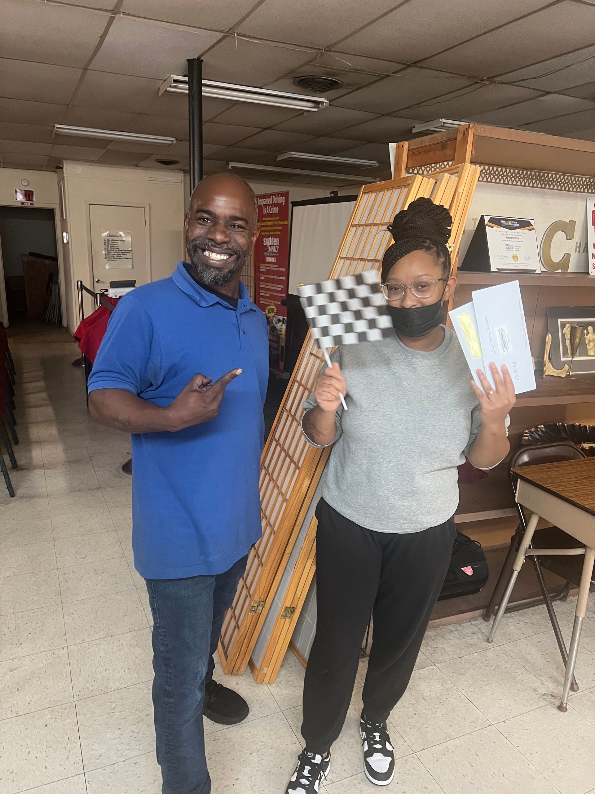A man and a woman are standing next to each other in a store holding a check and a checkered flag.