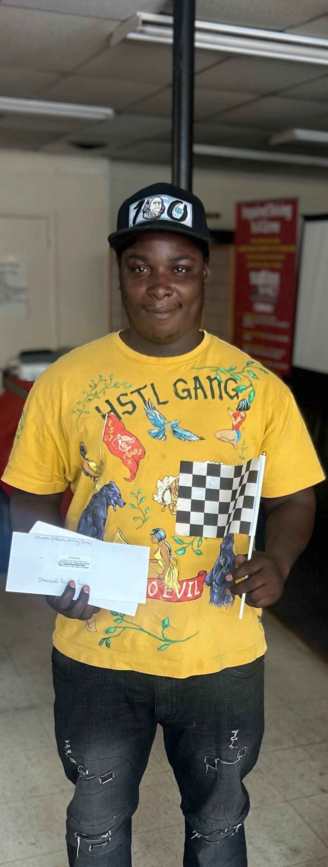 A man in a yellow shirt is holding a check and a checkered flag.