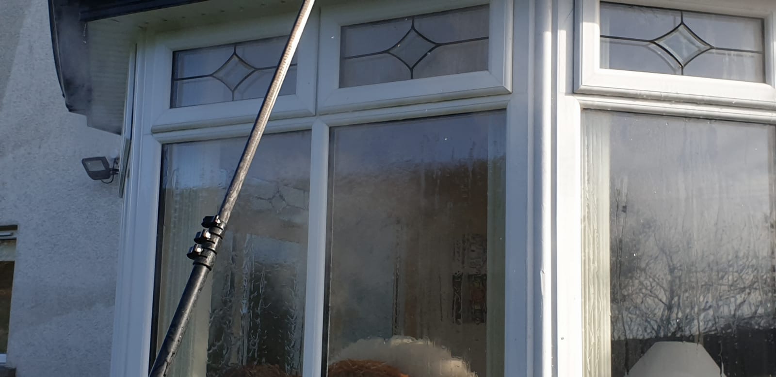 A man is cleaning a window with a high pressure washer.