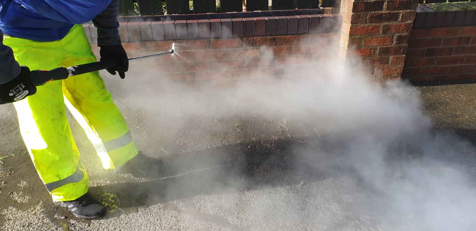 A man in yellow pants is using a high pressure washer to clean a driveway.