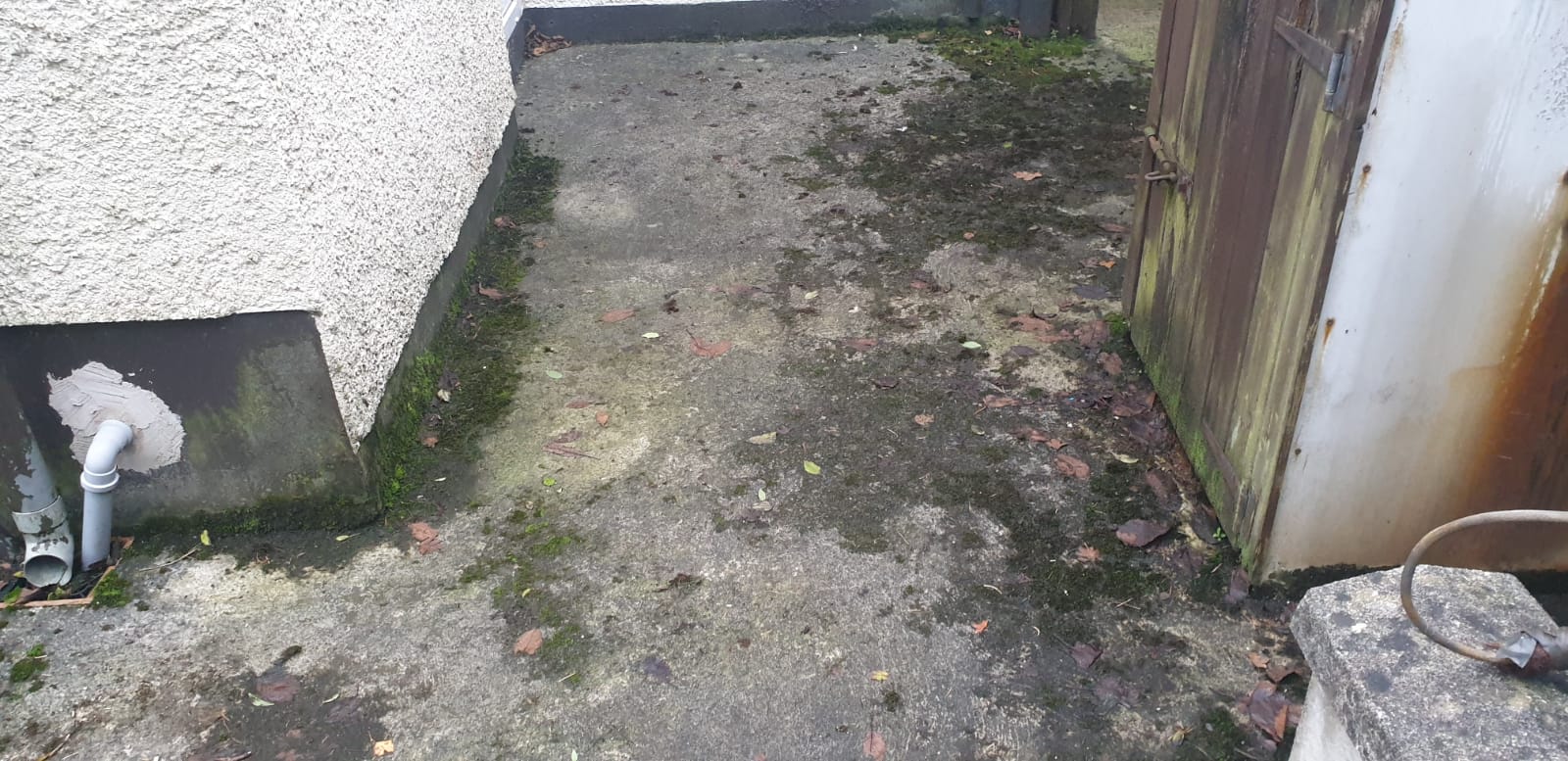 A dirty sidewalk next to a building with a hose coming out of it.