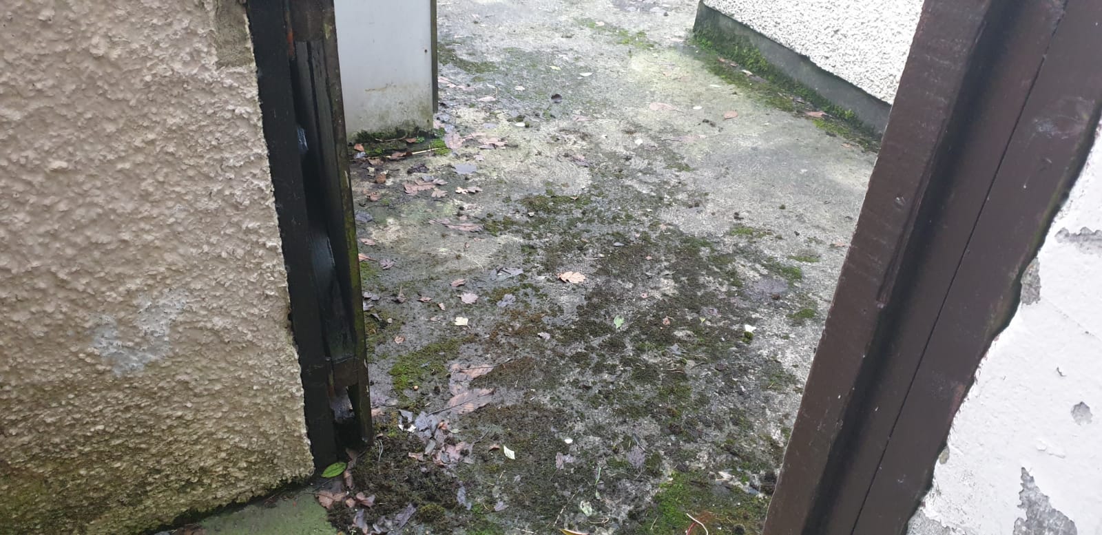 A dirty sidewalk next to a building with a wooden post.