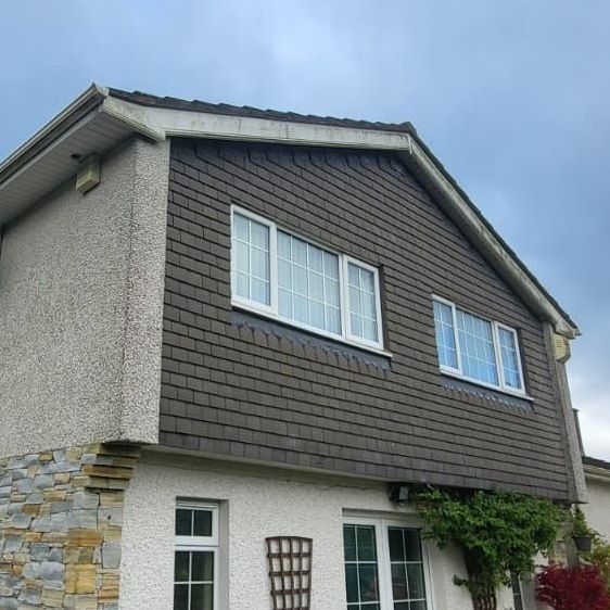 A house with brown siding and white windows against a cloudy sky