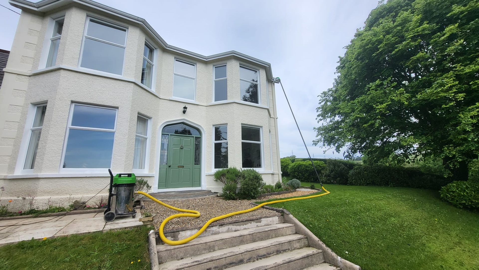 A large white house with a green door and a yellow hose in front of it.