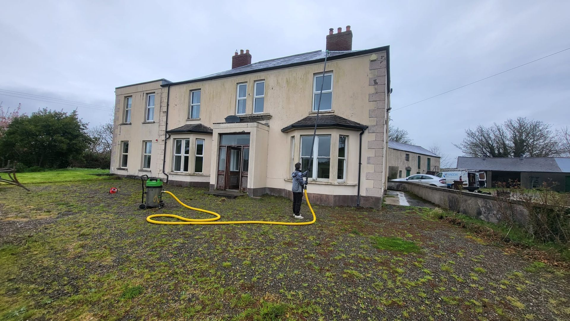 A man is standing in front of a large house with a yellow hose.