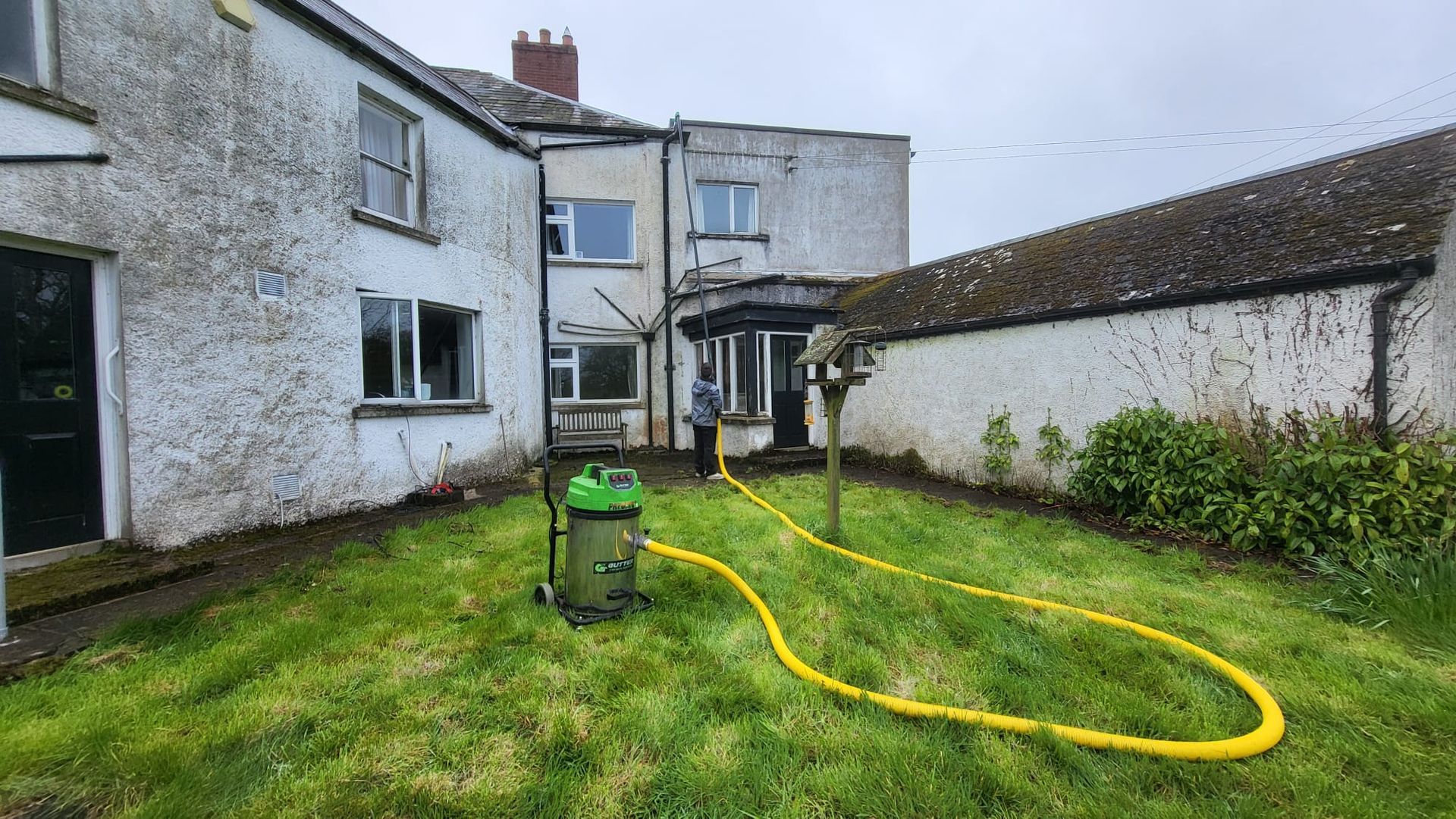 A gutter vacuum cleaner is sitting in the grass in front of a house.