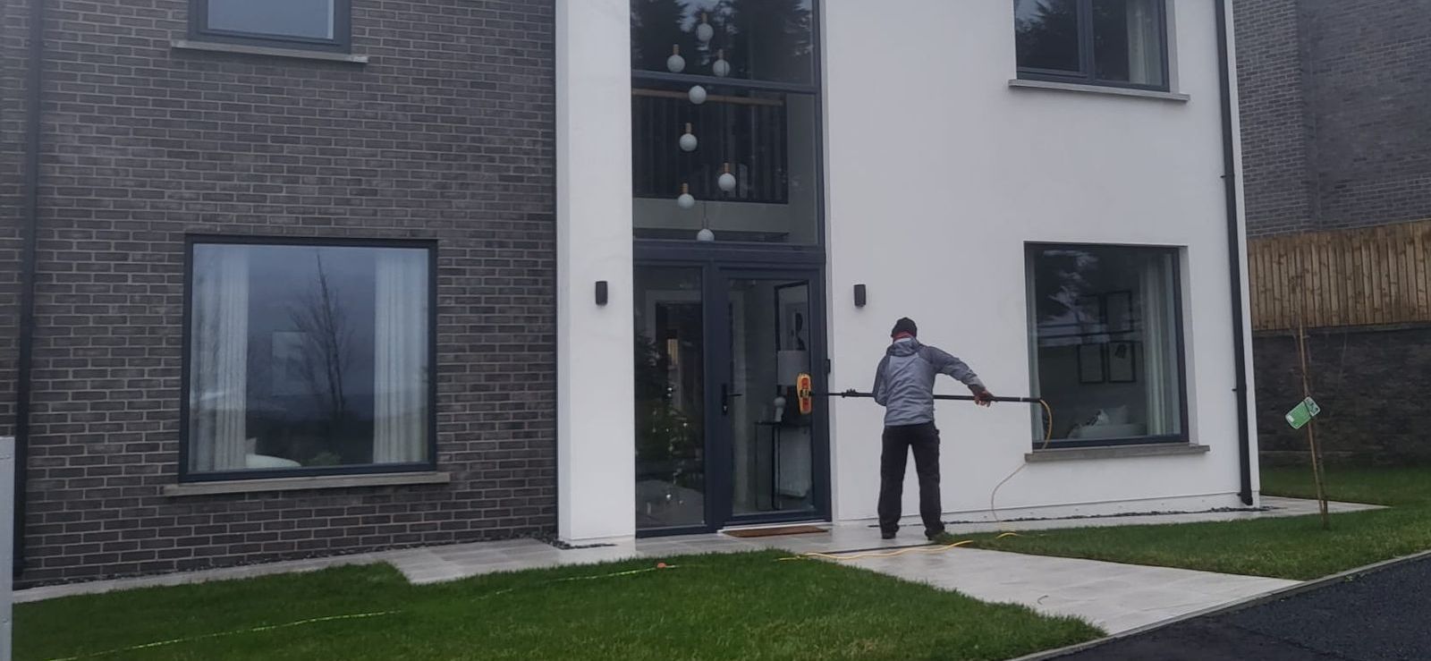A man is cleaning the windows of a house with a high pressure washer.