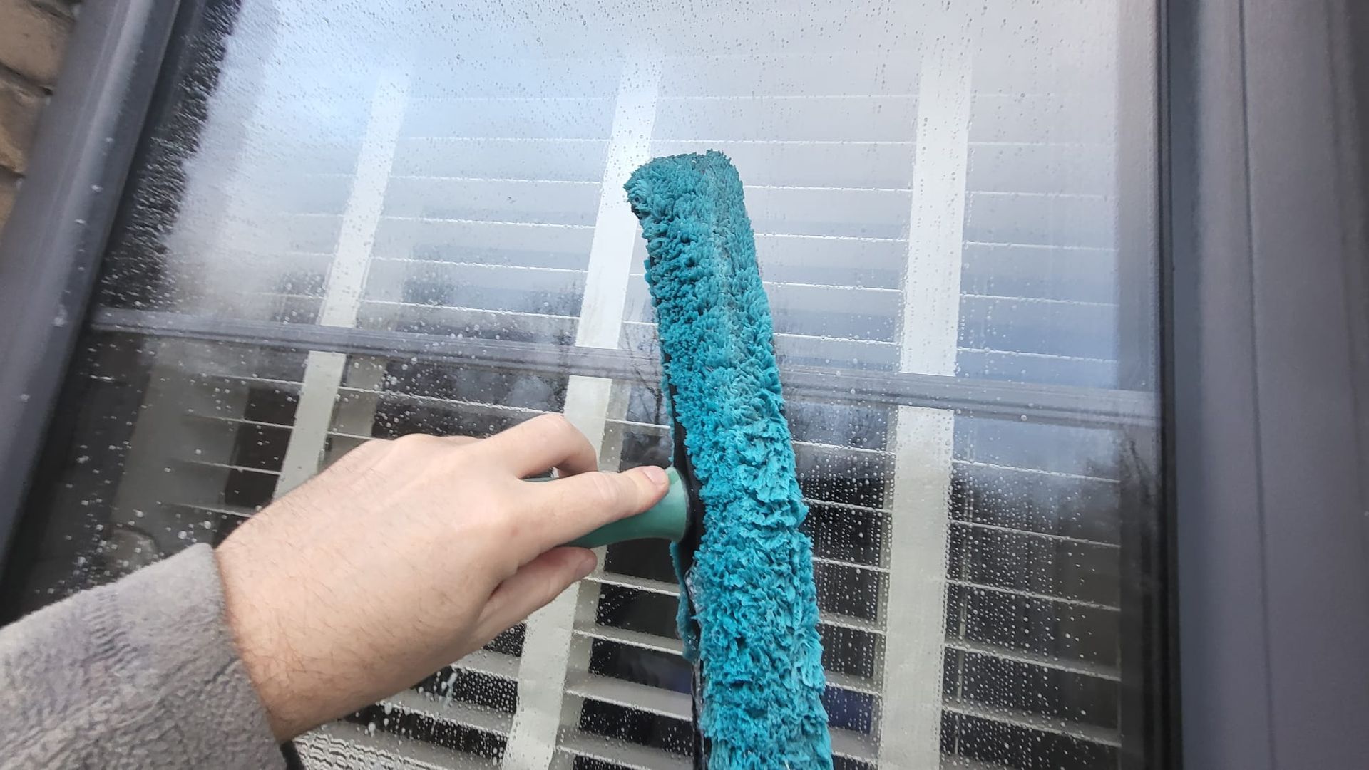 A person is cleaning a window with a blue brush.