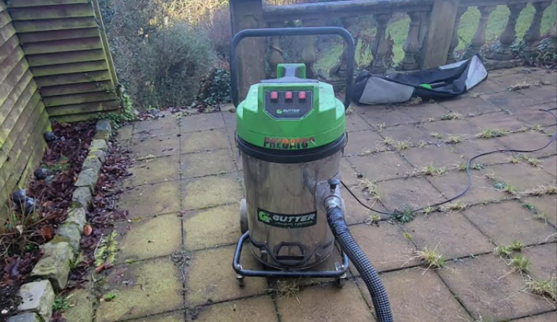 A green and silver vacuum cleaner is sitting on a patio.