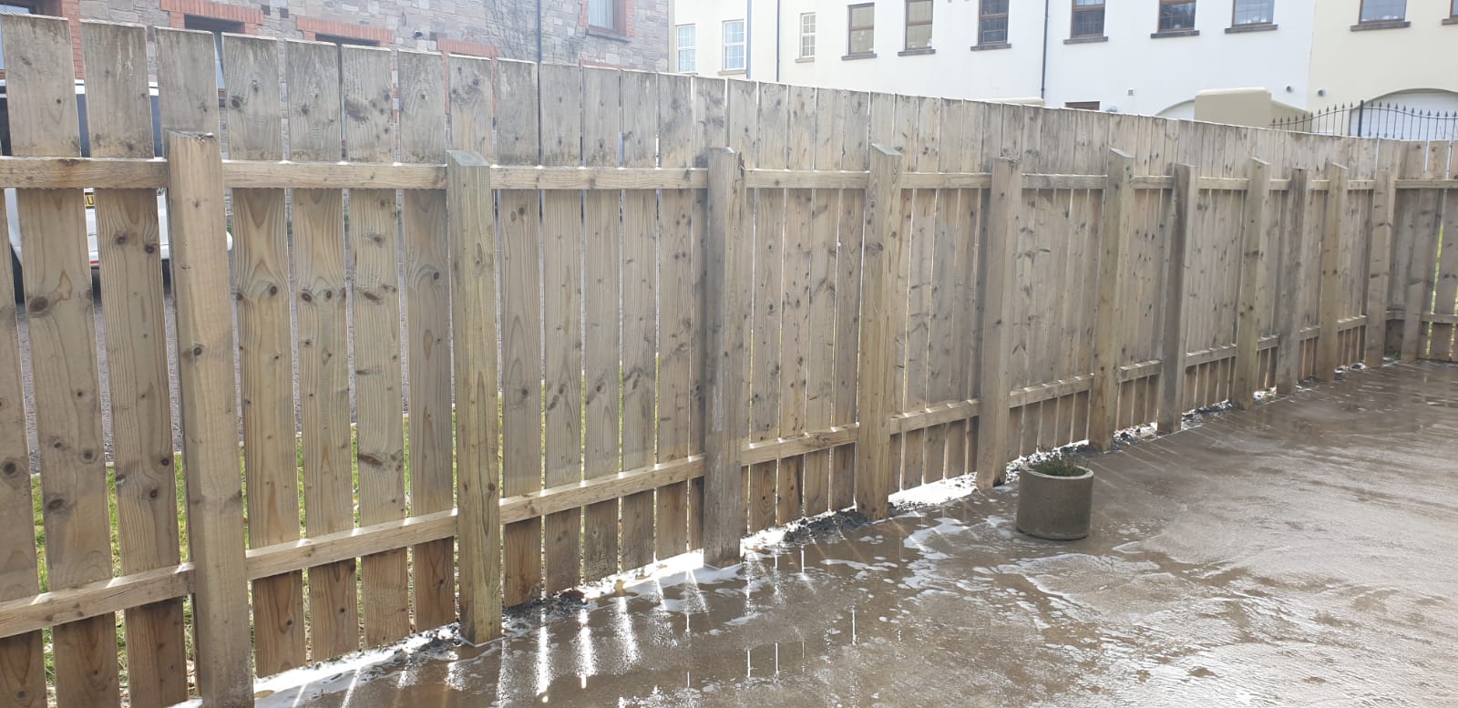 A wooden fence surrounds a muddy area in front of a building.