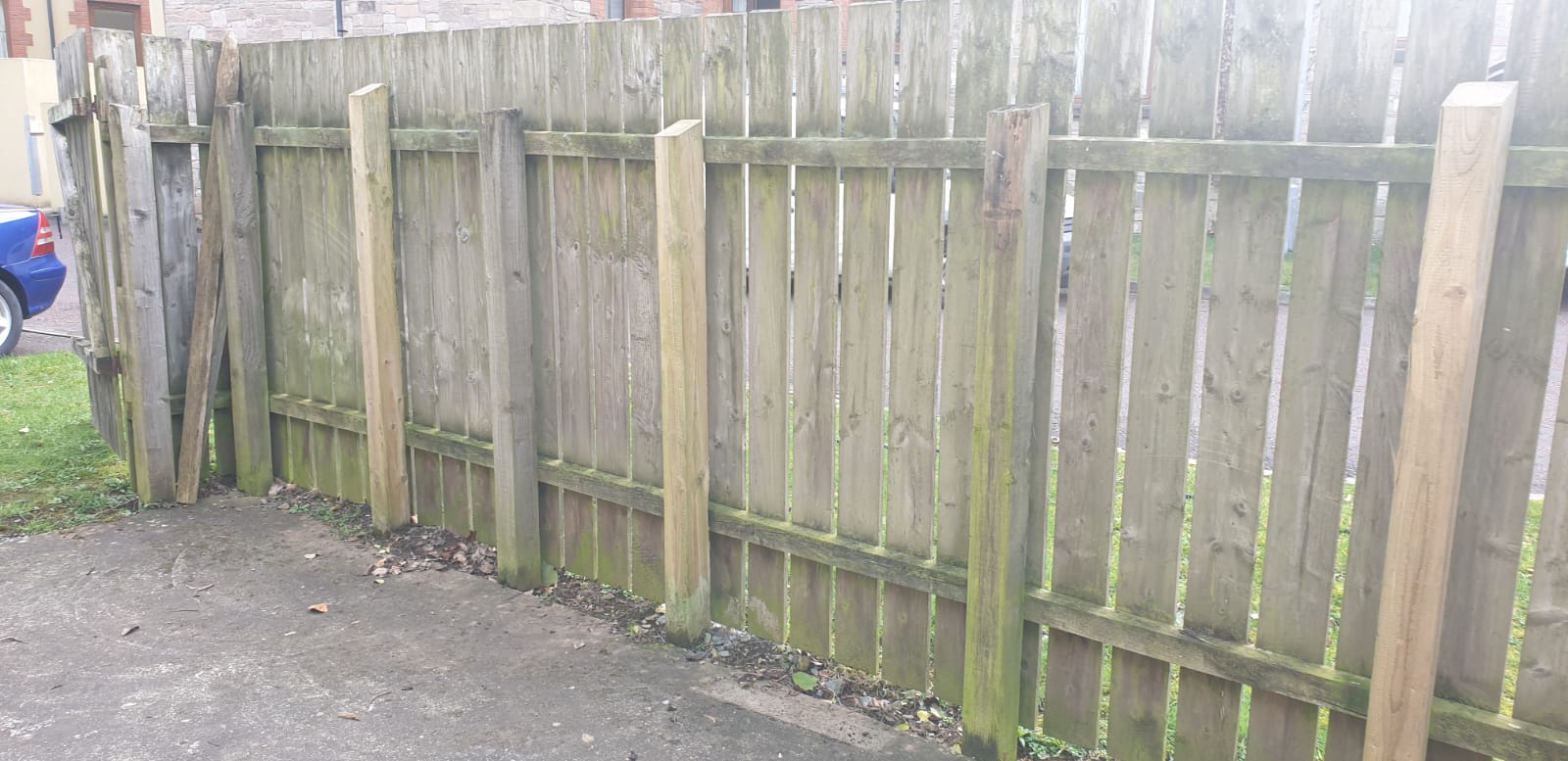 A wooden fence with a blue car parked behind it.