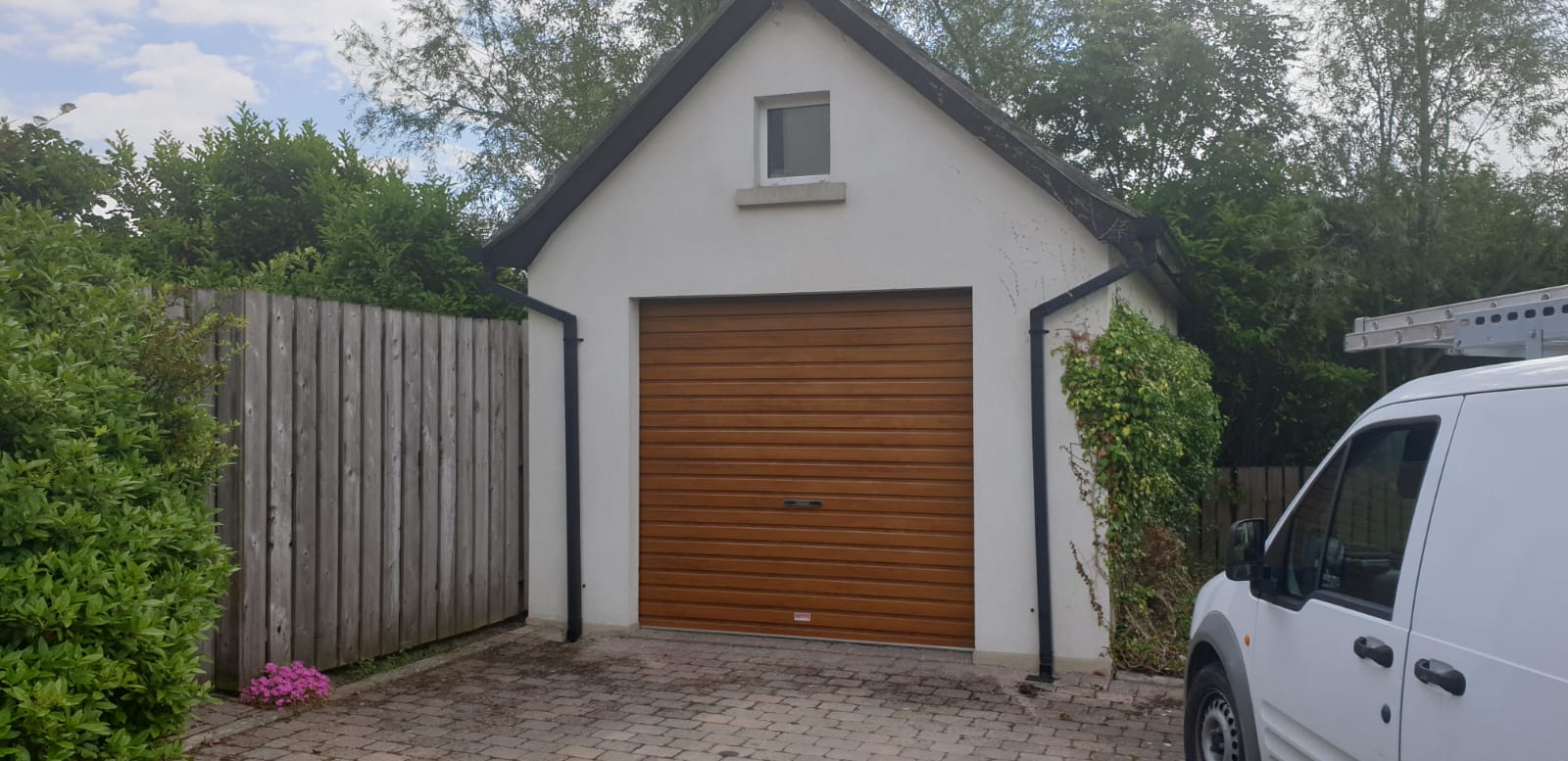 A white van is parked in front of a garage with a wooden door.