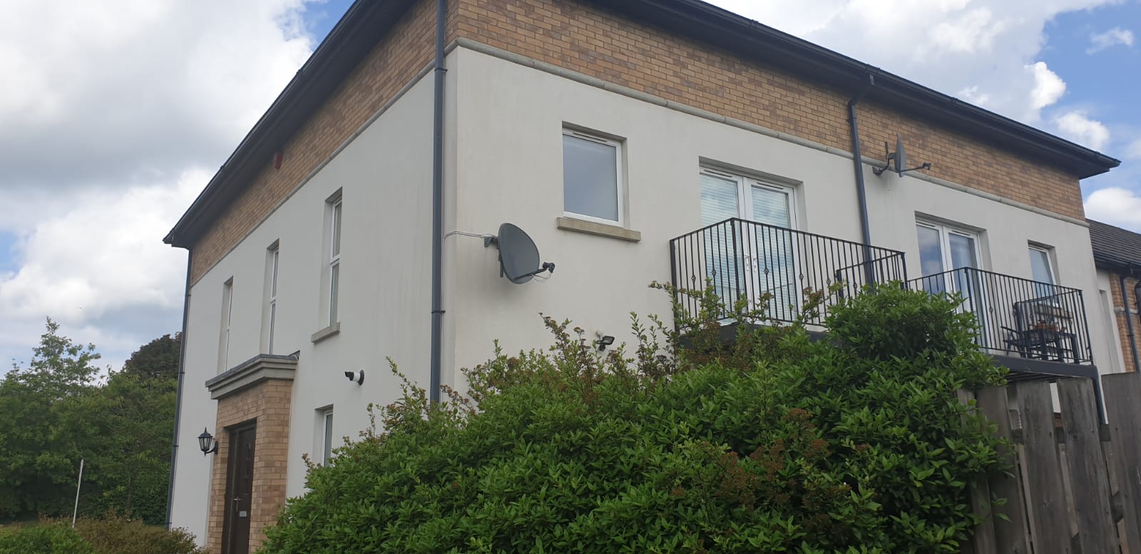 A large white house with a balcony and satellite dish on the side of it.