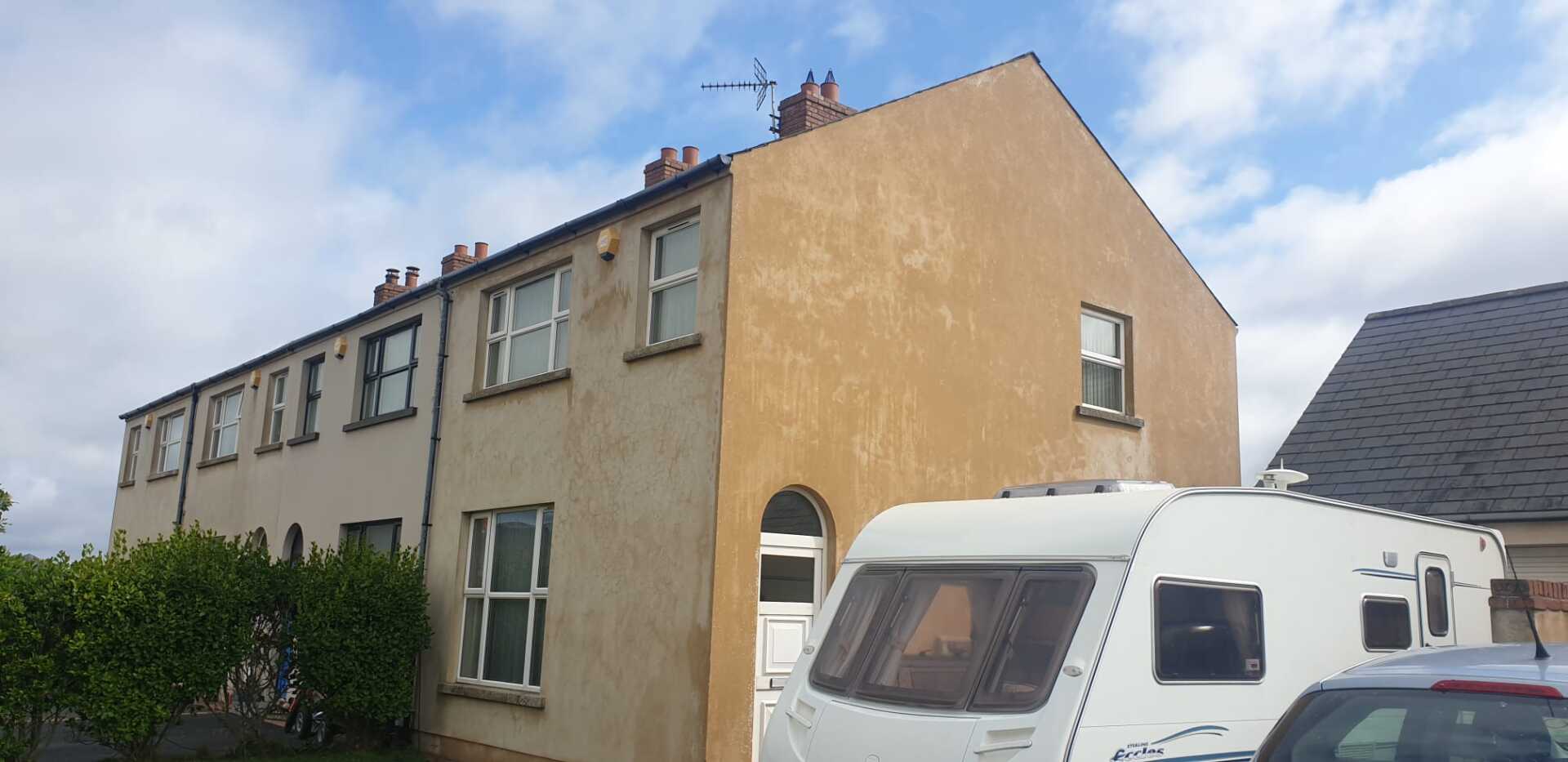 A white caravan is parked in front of a house.