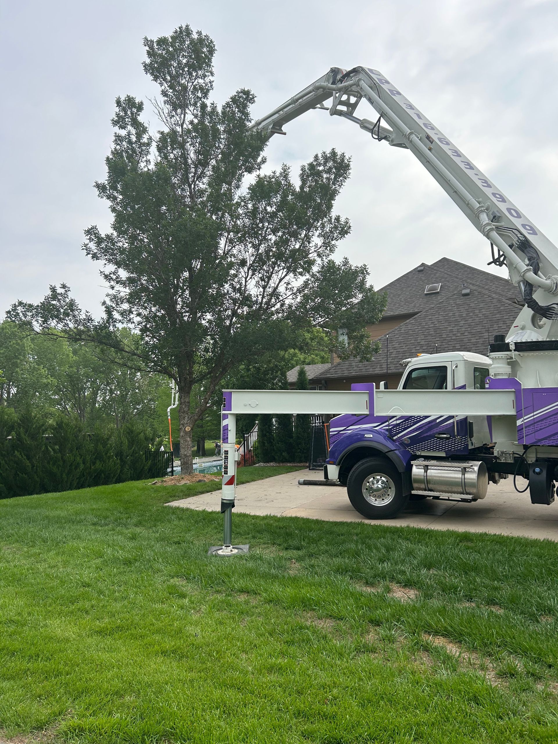 A purple and white concrete pump truck is parked in front of a house.