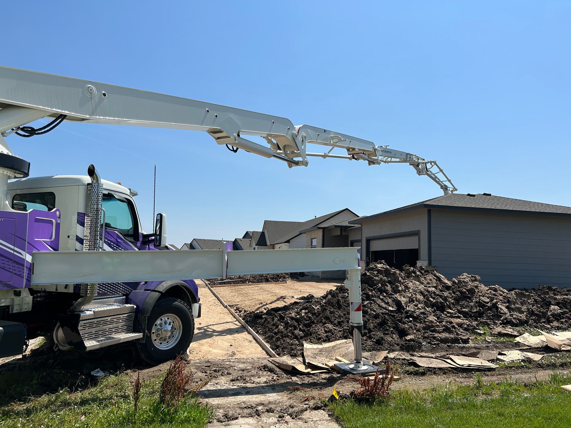 A purple and white truck is pumping concrete into a pile of dirt.