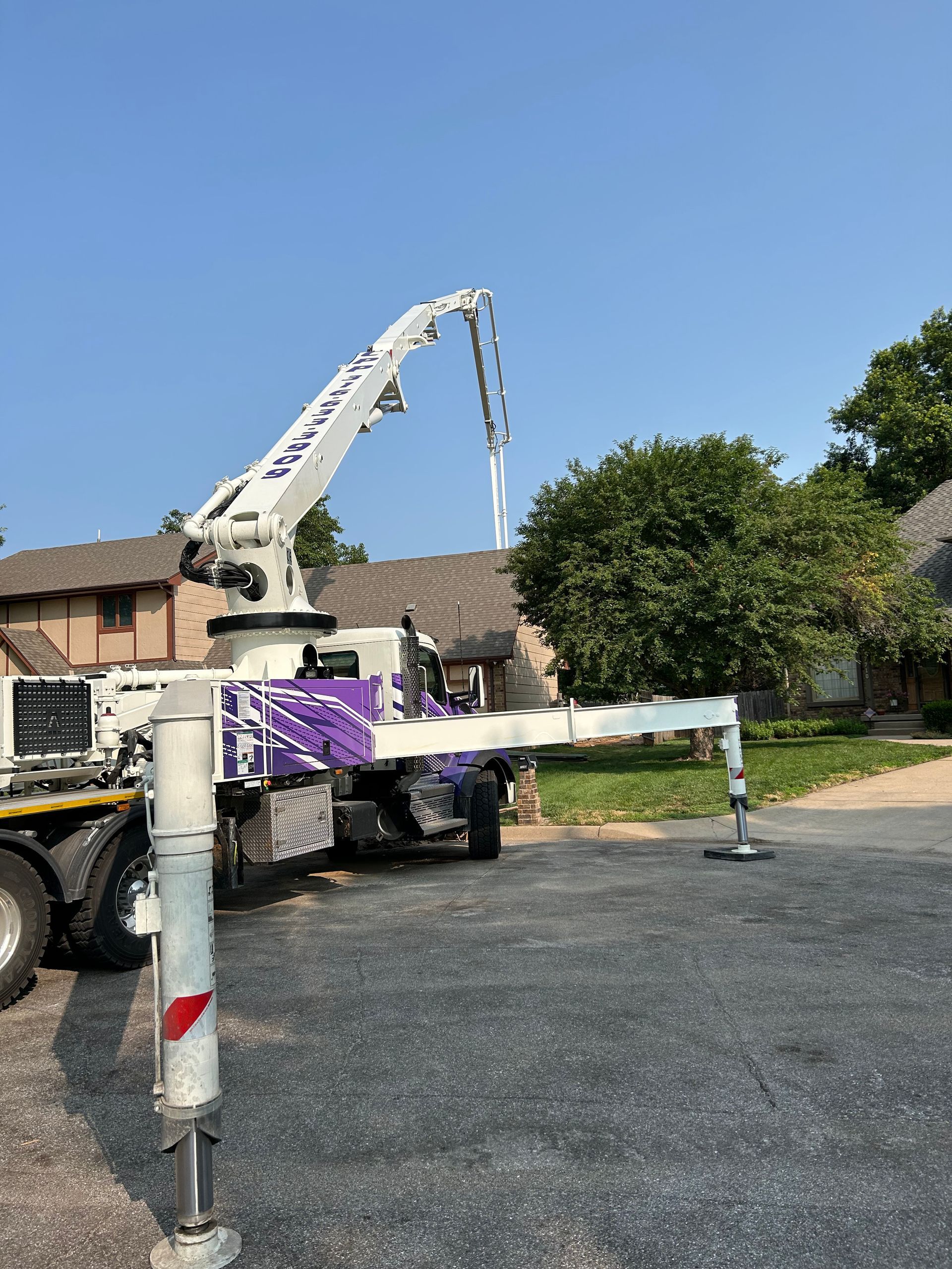 A white and purple concrete pump truck is parked in a parking lot.