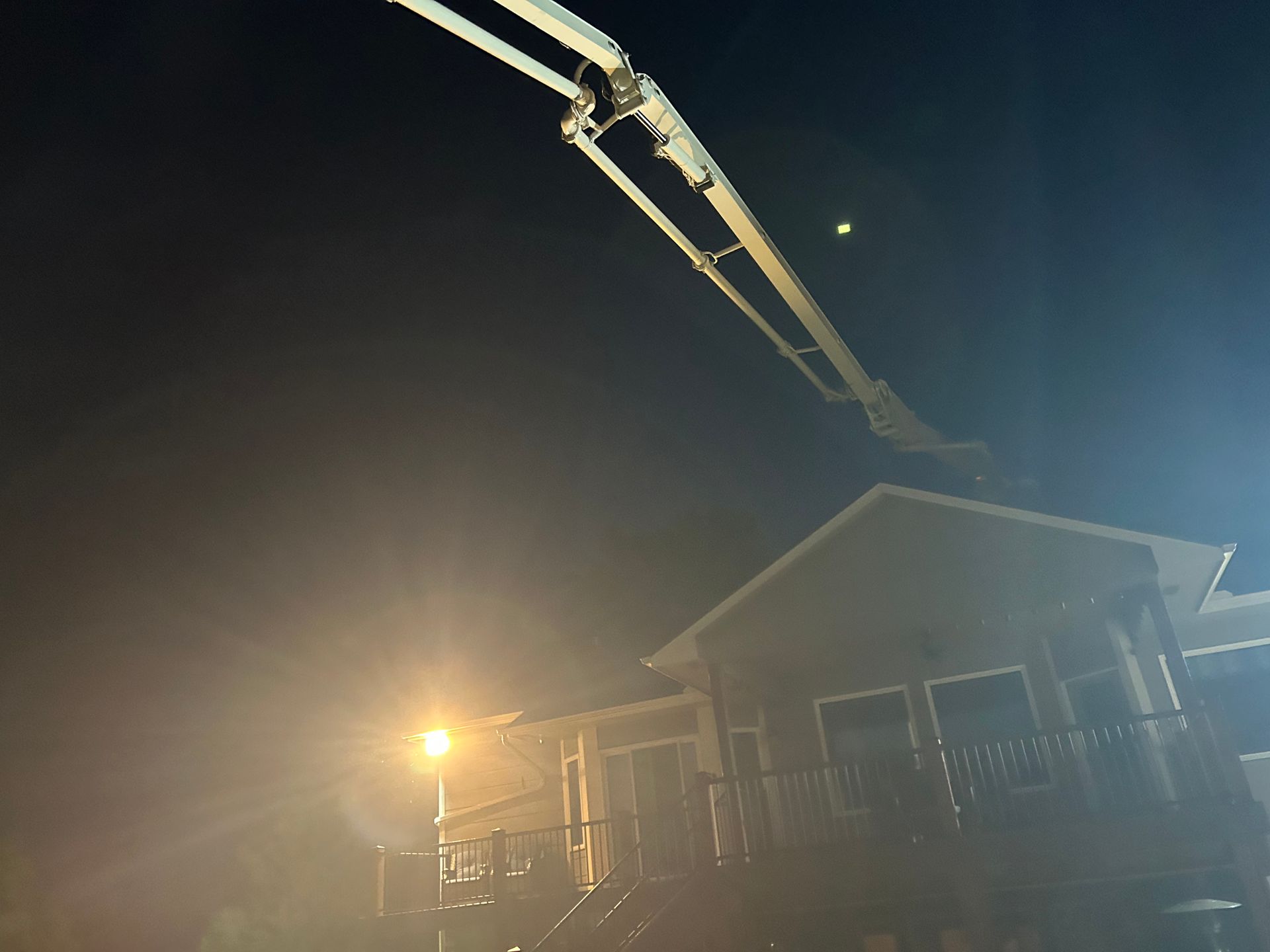 A concrete pump is being used to pour concrete into a house at night.