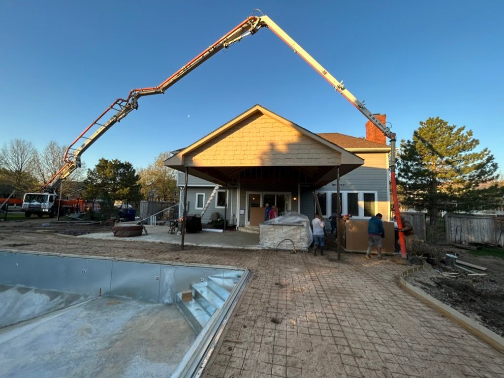 A concrete pump is being used to pour concrete into a pool in front of a house.