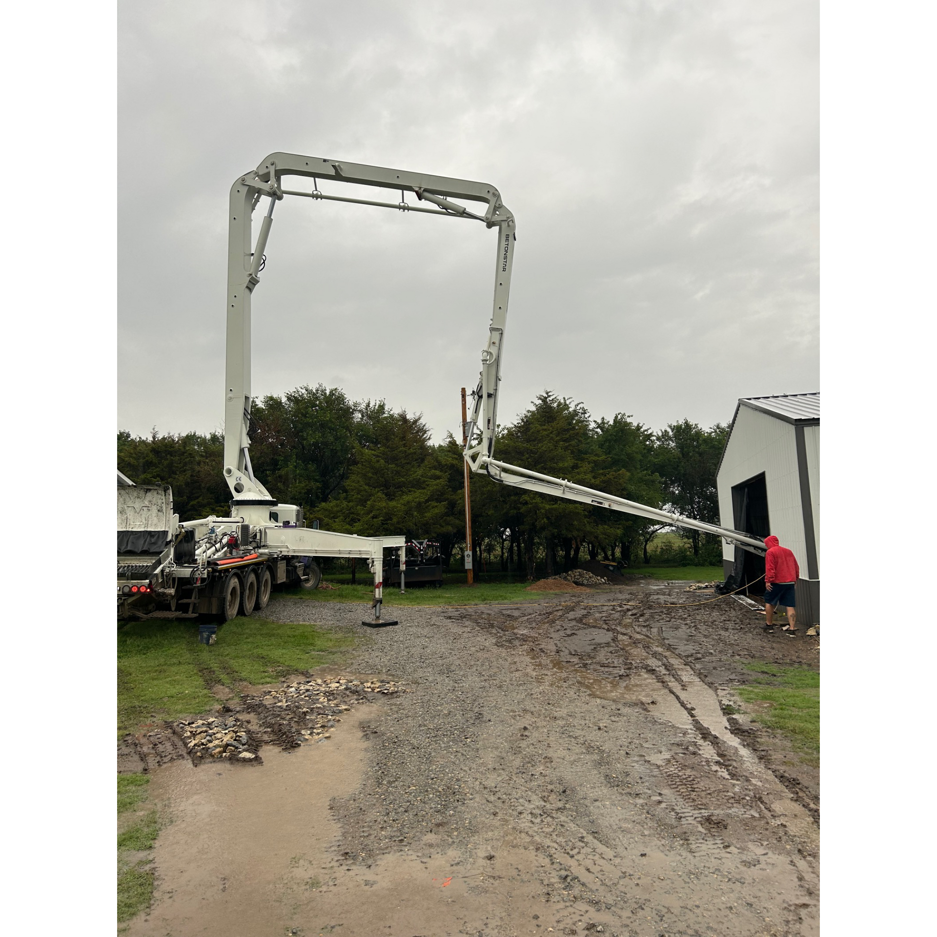 A concrete pump is being used to pump concrete into a muddy driveway.
