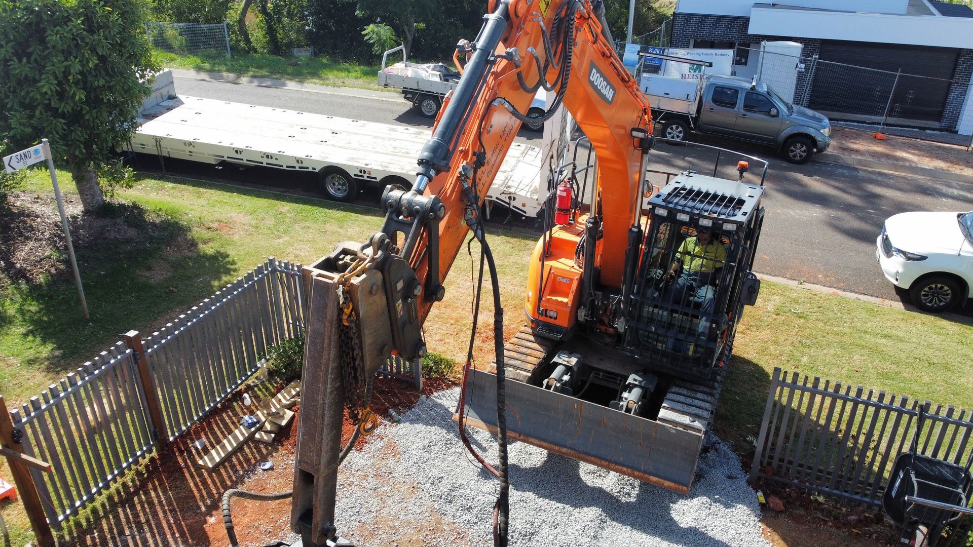 A Large Orange Excavator Is Digging The Ground In Front Of A Fence — Southeast QLD — East Coast Group of Companies