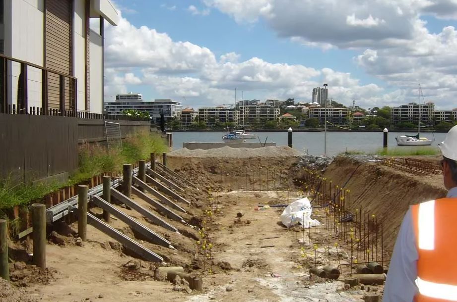 Deep foundation works with steel supports and timber piles at a riverside building site.