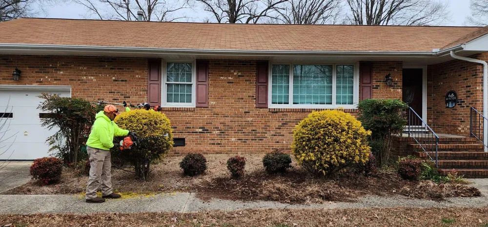 A man is cutting bushes in front of a brick house.