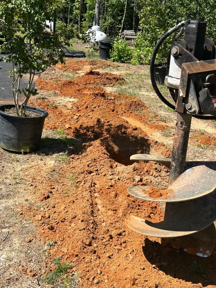 A machine is digging a hole in the ground next to a potted plant.
