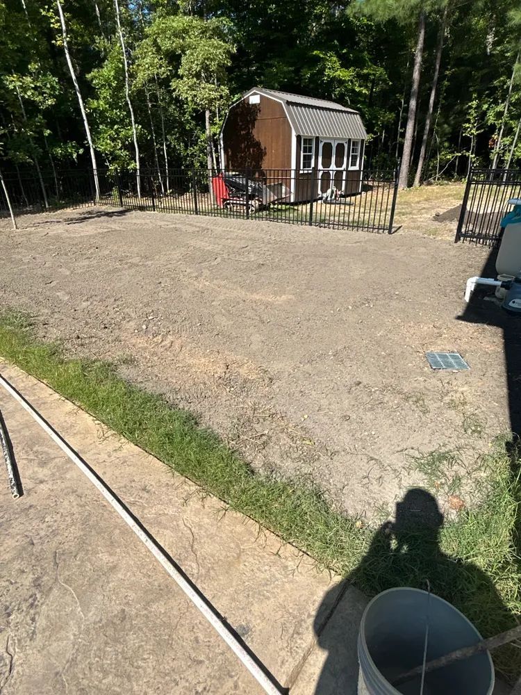 A shed is sitting in the middle of a dirt field next to a fence.