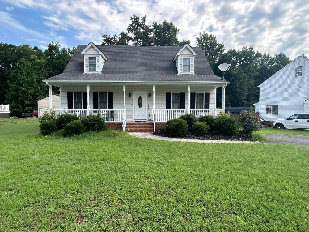 A white house with a porch and a car parked in front of it.