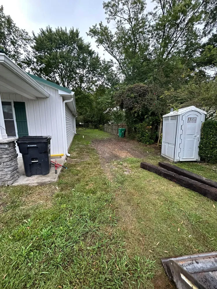A portable toilet is sitting in the grass next to a house.