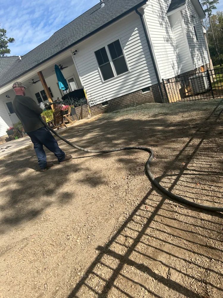 A man is cleaning a driveway with a hose in front of a house.