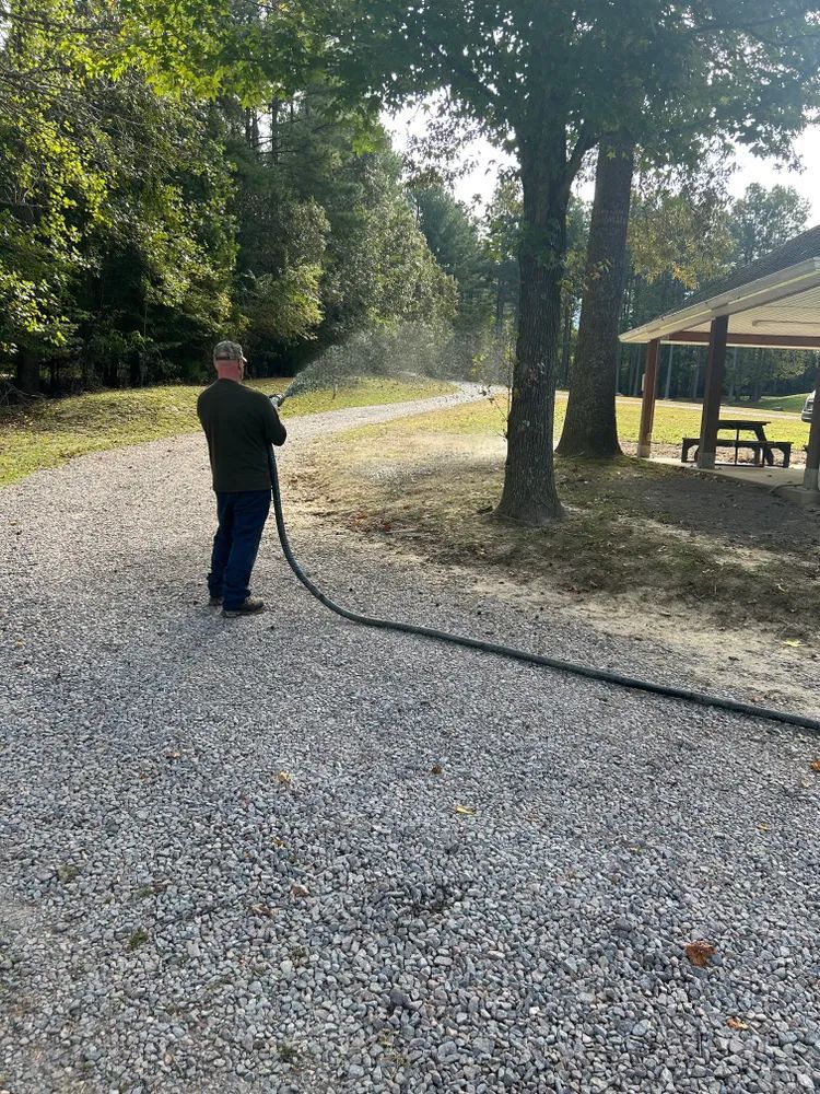 A man is spraying water from a hose on a gravel road.