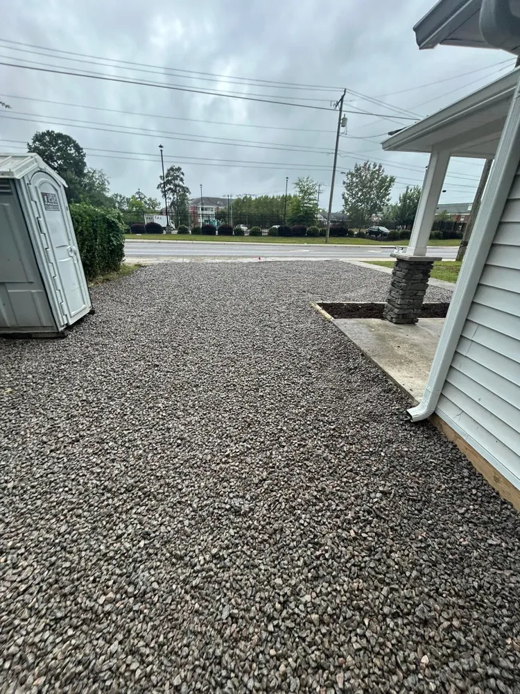 A gravel driveway leading to a house with a shed in the background.
