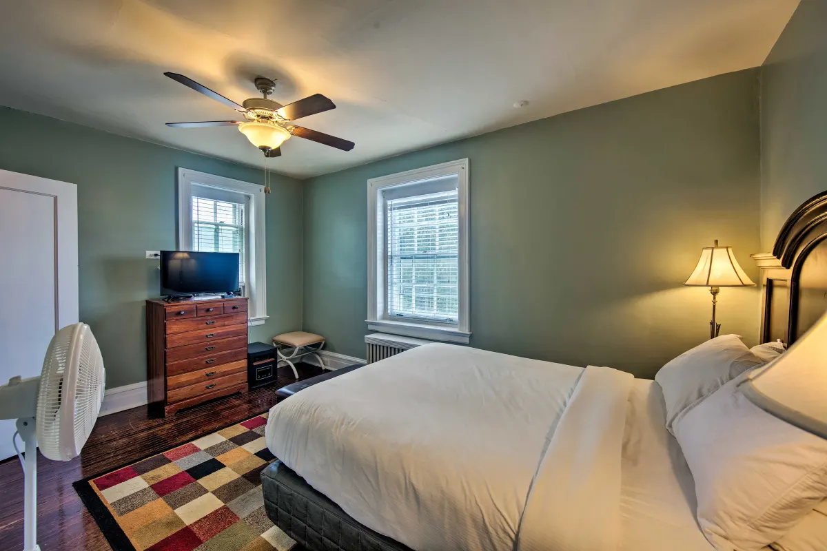 A bedroom with a bed , dresser , television and ceiling fan.