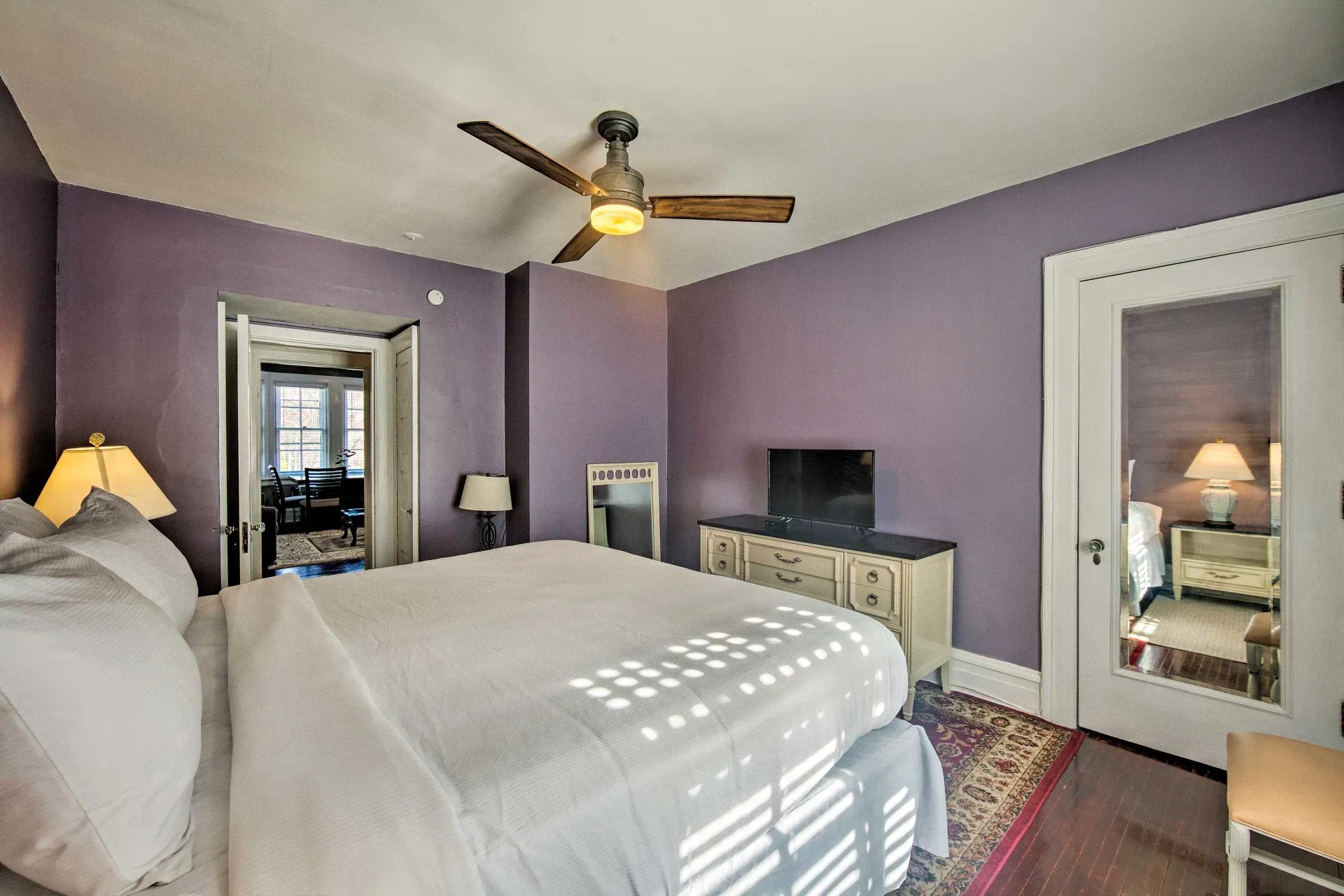 A bedroom with purple walls and a ceiling fan