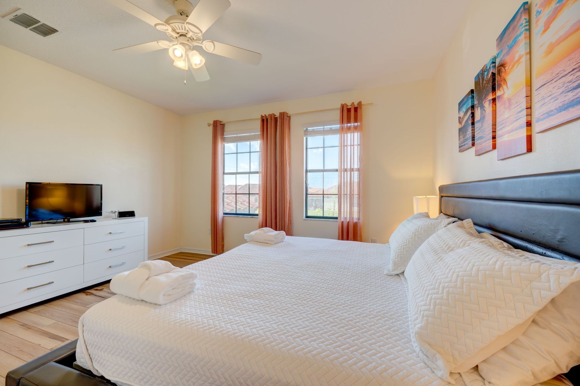 A bedroom with a king size bed , dresser , television and ceiling fan.