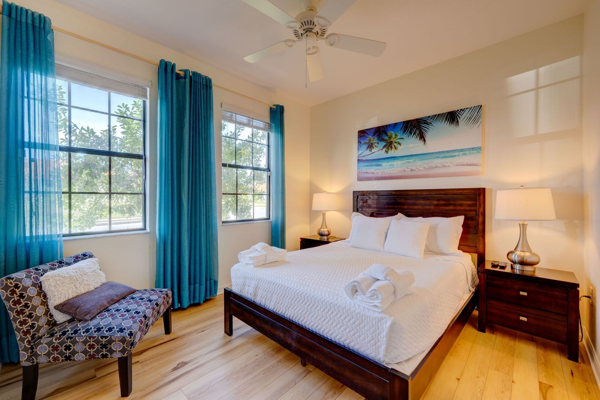 A bedroom with a king size bed , two nightstands , a chair , and a ceiling fan.