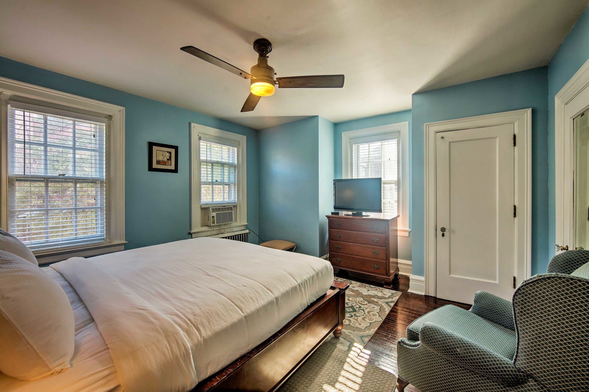 A bedroom with a bed , chair , dresser , television and ceiling fan.