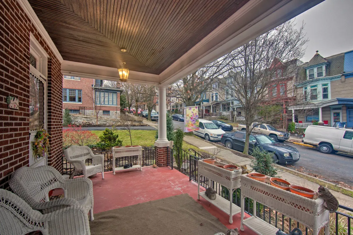A porch with wicker chairs and a bench in front of a brick house.