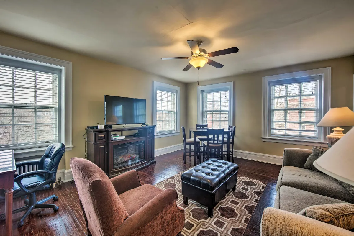 A living room with a couch , chair , television , fireplace and ceiling fan.