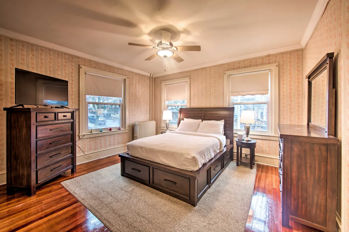 A bedroom with a bed , dresser , television and ceiling fan.