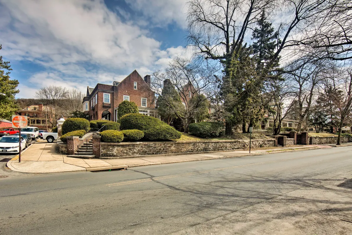 A large brick house is sitting on the corner of a street surrounded by trees.