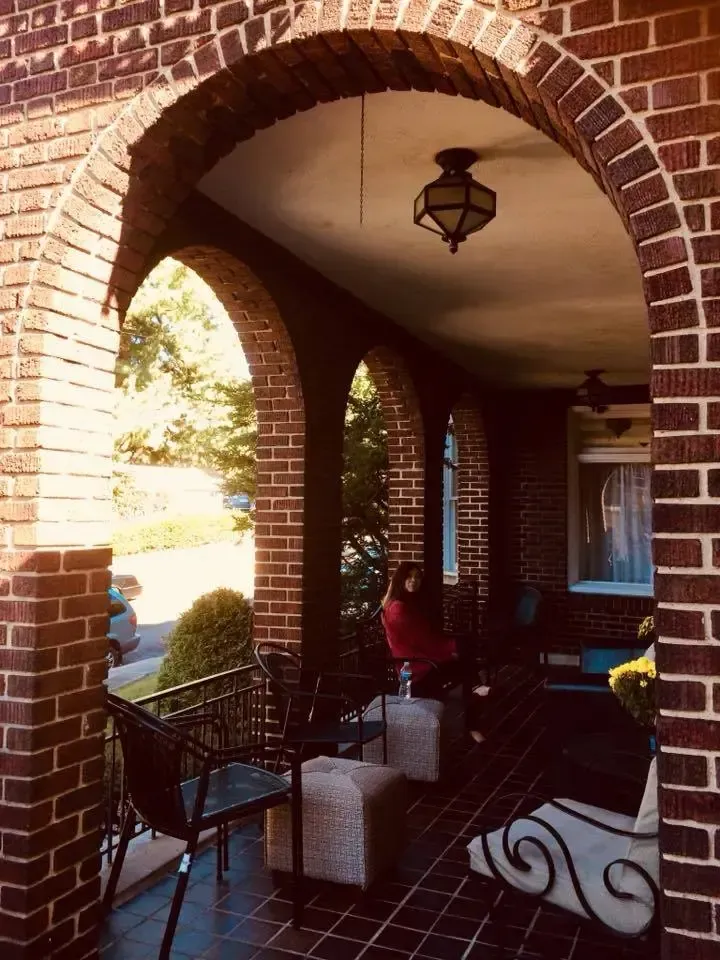 A woman sits on the porch of a brick house