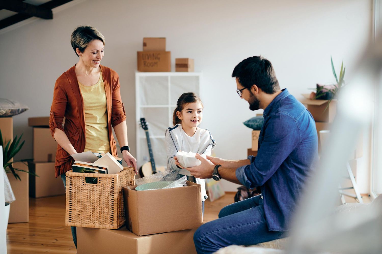 Family unpacking boxes in a new home; woman in orange, man in blue, girl with a box; cardboard boxes in the background. Parental Relocation in Nashville, Tennessee