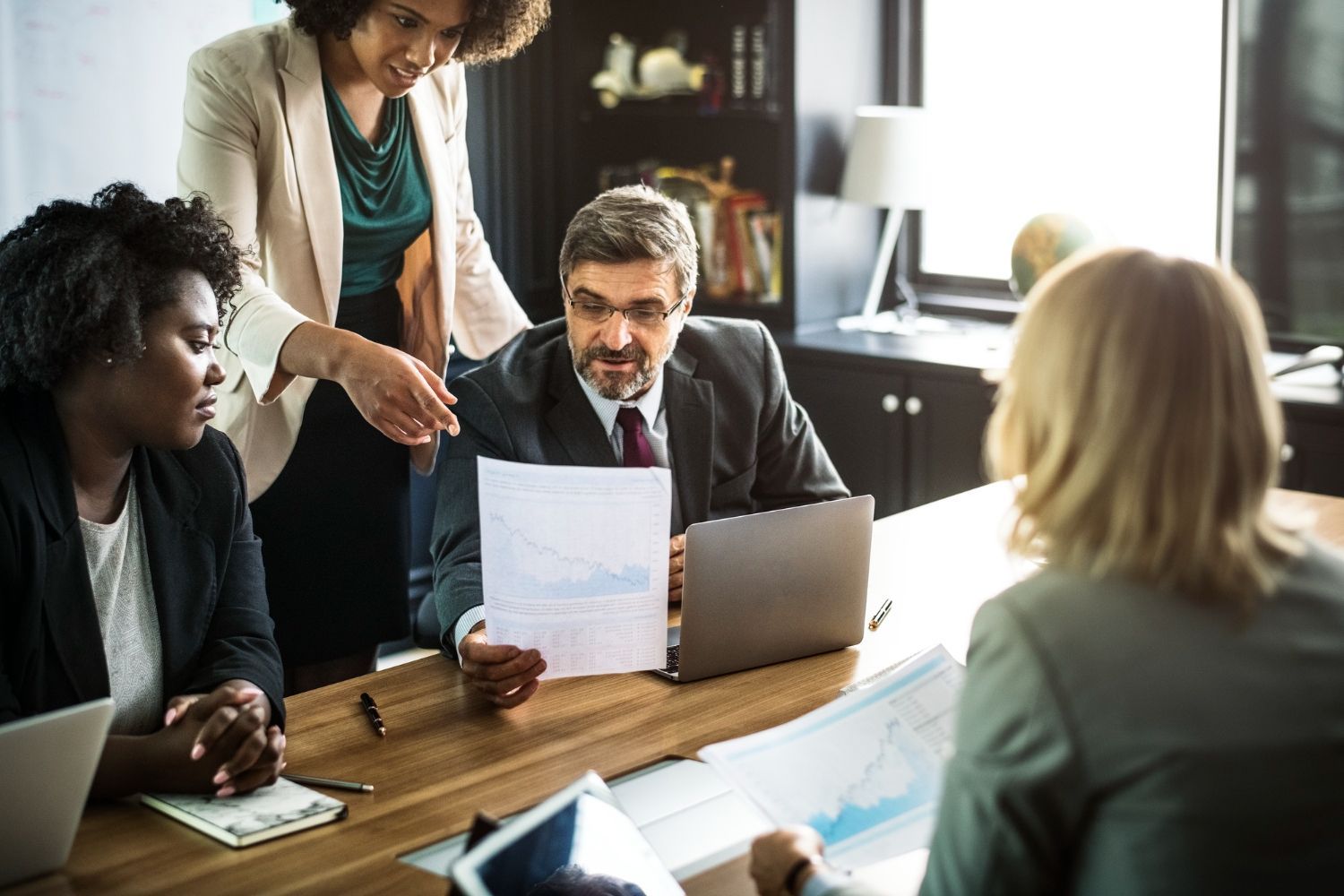 Business team at a wooden table reviewing charts; woman pointing, laptop open. Corporation/LLC Issues in Nashville, Tennessee