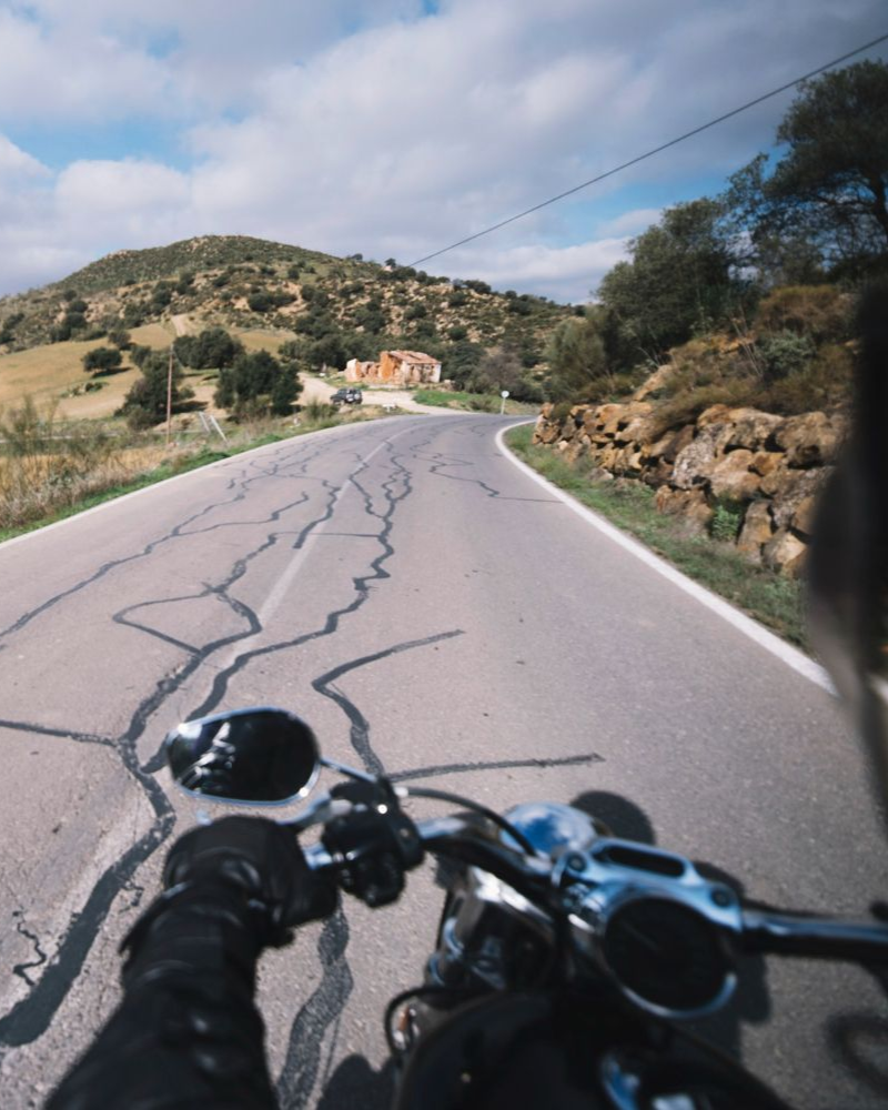 Motorcycle rider on a winding road with cracked pavement, a mountain in the background. Sunny day. Motorcycle Accidents in Nashville, Tennessee