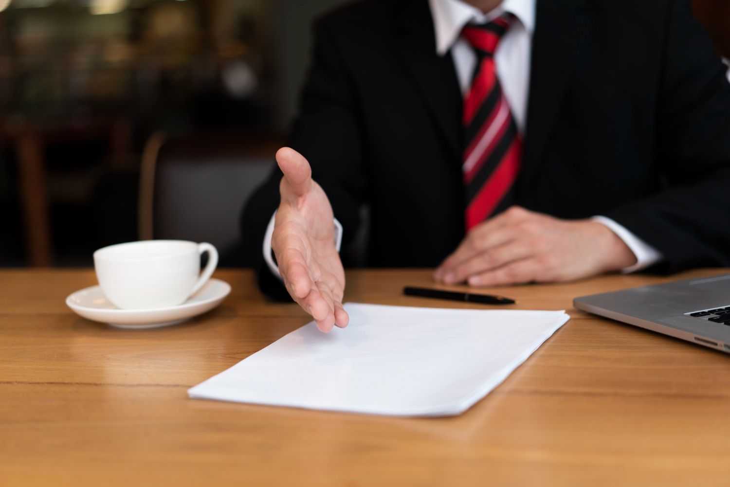 Person in suit extends hand over a blank document on a wooden table. Breach of Contract in Nashville, Tennessee