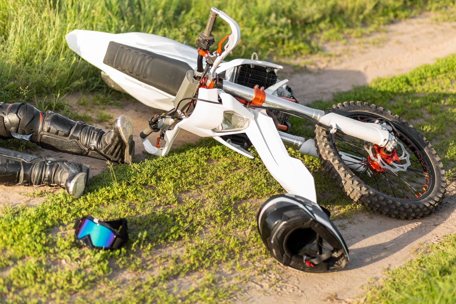 White dirt bike crashed on grassy ground, helmet, knee pads nearby. Motorcycle Accidents in Nashville, Tennessee